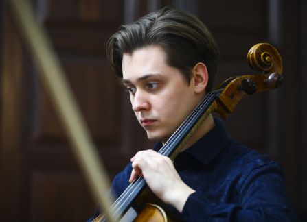 fotografia. Koncert we wnętrzu Willi Decjusza. Mężczyzna w granatowej koszuli gra na wiolonczeli.